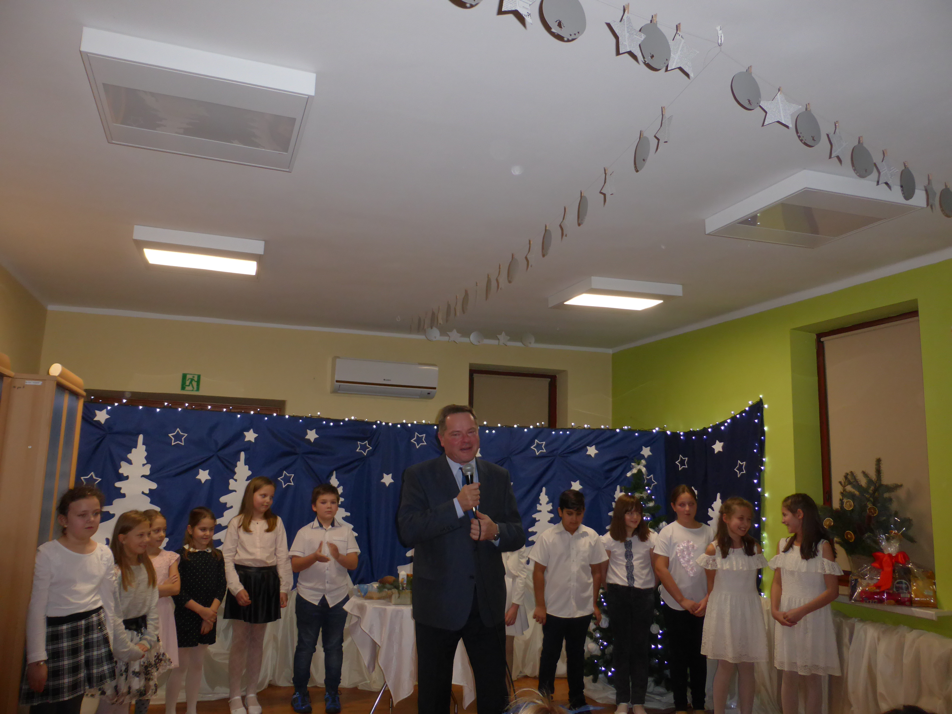 Na zdjęciu dzieci na tle dekoracji, przed nimi przemawia przewodniczący Rady Miejskiej w Andrychowie Krzysztof Kubień