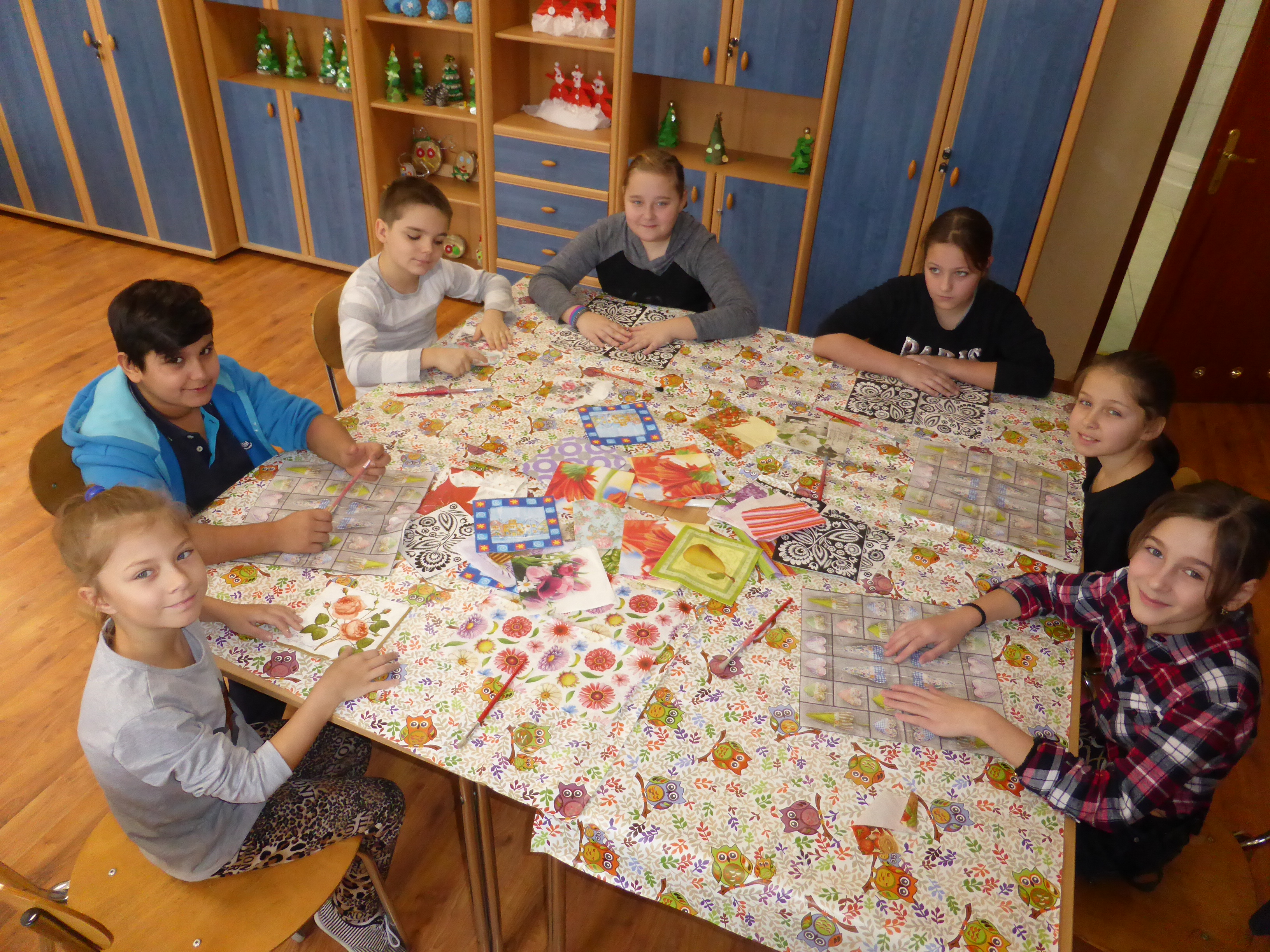 Na zdjęciu dzieci siedzące przy stole, na którym leżą serwetki do decoupage