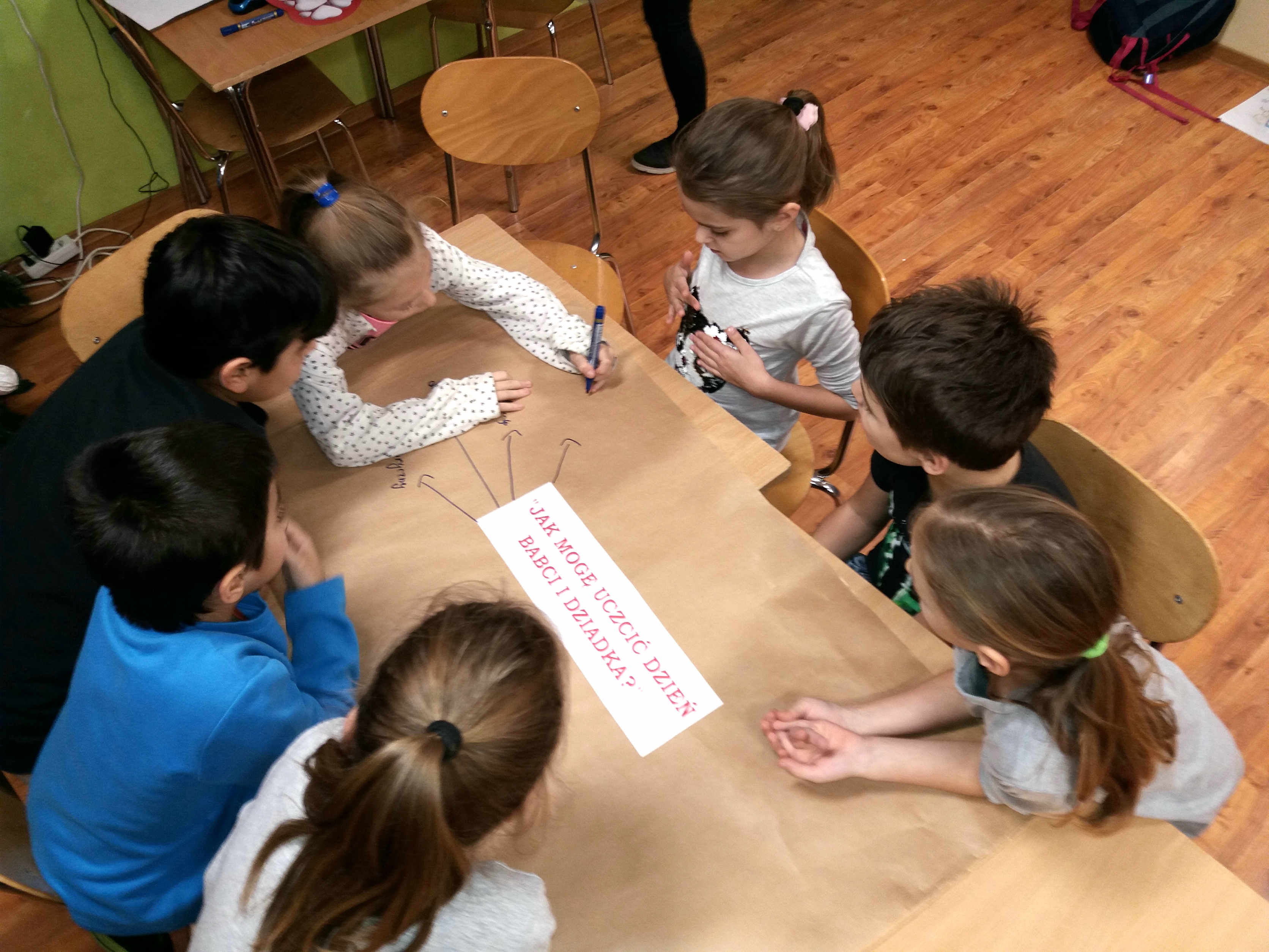 Na zdjęciu dzieci zapisują odpowiedzi na pytanie: "Jak mogę uczcić Dzień Babci i Dziadka?"