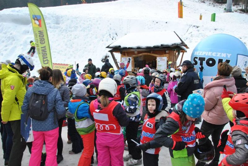 Dzieci w kaskach narciarskich, obok policjant, w tle stok narciarski.