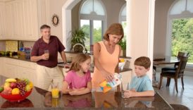 Dzieci z rodzicami w kuchni, mama nalewa dzieciom sok z kartonu do szklanek