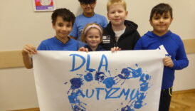Dzieci trzymają kartkę papieru z niebieskim sercem, składającym się z odbitych dłoni i napisem "Dla autyzmu"