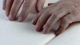 zbliżenie na ręce osoby, która czyta tekst napisany języku Braille'a