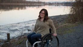 Uśmiechnięta kobieta na wózku inwalidzkim, w tle rzeka lub jezioro