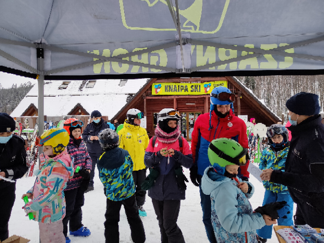 Dzieci i dorośli gromadzą się wokół policjantki, są zainteresowani tematem bezpieczeństwa na stoku narciarskim