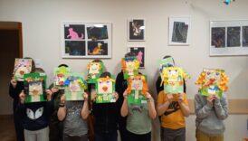 Dzieci pozują do zdjęcia grupowego, zasłaniając sobie twarz, wykonaną przez siebie pracą plastyczną