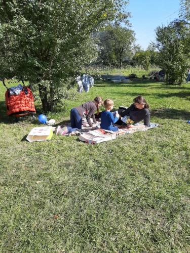 Uczestnicy pikniku siedzą na kocu w ogrodzie
