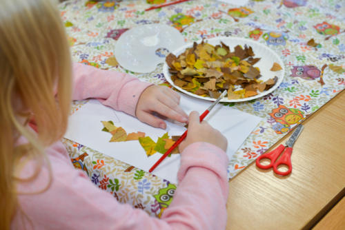 Dziewczynka przykleja fragmenty liści do kartki papieru