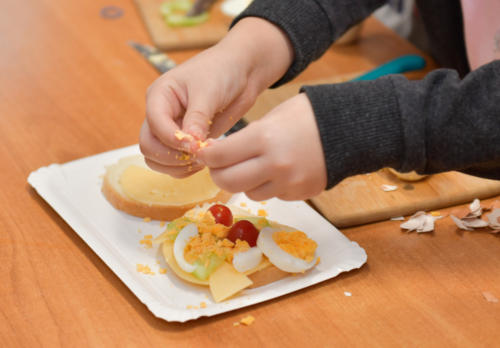 Zbliżenie na ręce dziecka, które ozdabia kanapkę jajkiem i pomidorkami