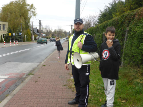 Policjant, obok niego chłopiec, który wykrzykuje hasła zachęcające do trzeźwości na drogach