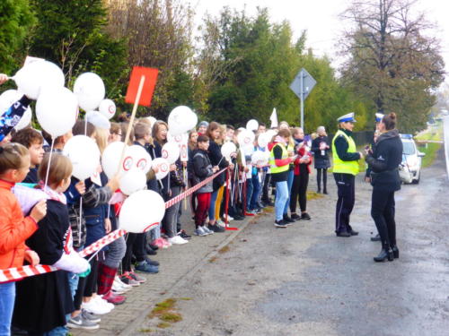 Dzieci stoją przy drodze z balonami z logo kampanii "No promil - no problem". Obok policjanci i organizatorzy.