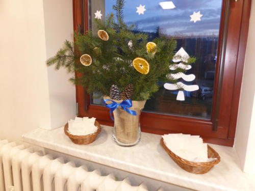 Stroik świąteczny - gałązki ozdobione szyszkami i plastrami suszonej pomarańczy, po dwóch stronach talerzyki z opłatkami
