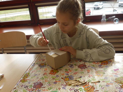 Dziewczynka ozdabia papierowy domek zapałkami