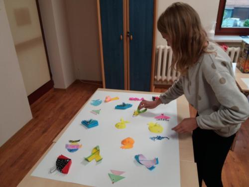 Dziewczynka przykleja przestrzenne rybki z papieru do dużej kartki