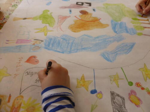 Kartka papieru i ręce dzieci - jedna rysuje kredką drzewa, druga pisze napis "Segreguję śmieci"