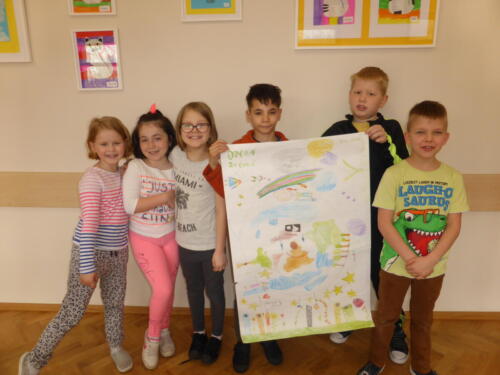 Dzieci prezentują plakat z napisem "Dzień Ziemi". Na plakacie rysunek uśmiechniętej planety Ziemi, drzew, koszy do segregowania odpadów
