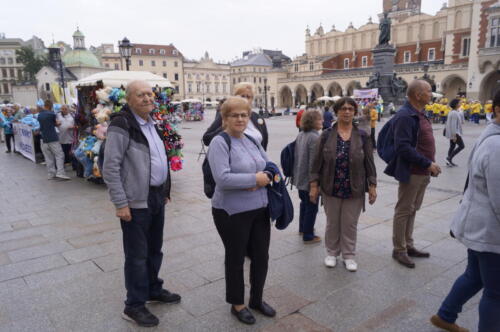 seniorzy stoją na Rynku Głównym w Krakowie, w tle pomnik Adama Mickiewicza i Sukiennice
