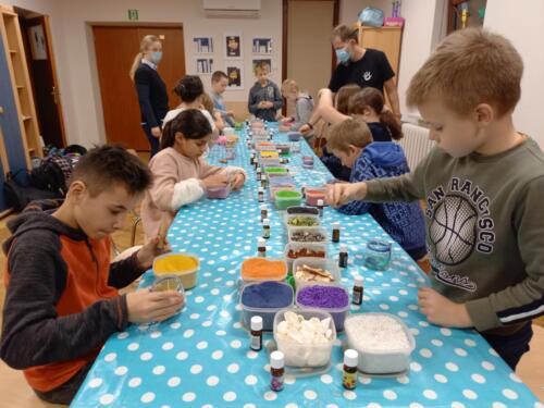 Dzieci siedzą przy stole i wsypują kolorowy piasek do słoiczków