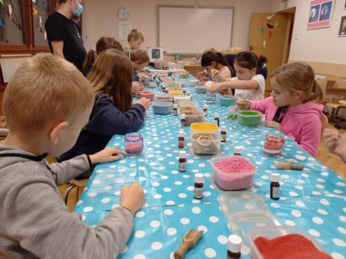 Dzieci tworzą kolorowe świeczki, wsypują do słoiczków kolorowy piasek i kamyczki
