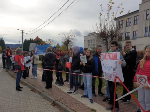 Dzieci stoją na chodniku wzdłuż drogi, trzymają tabliczki z logo kampanii No promil - no problem