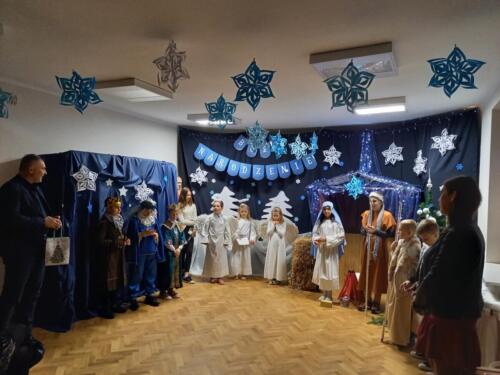 Dzieci i dwójka osób dorosłych stoją na tle dekoracji świątecznej 