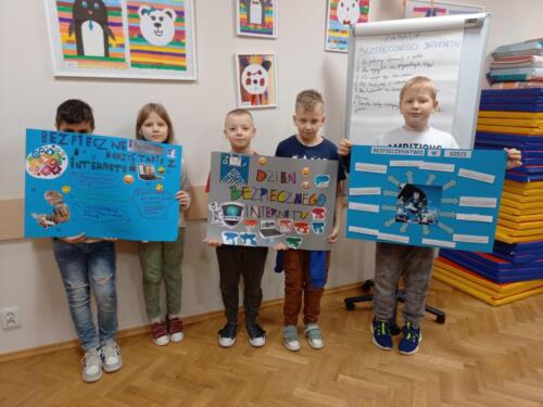 Dzieci pozują do zdjęcia grupowego, trzymają w rękach stworzone przez siebie plakaty z okazji Dnia Bezpiecznego Internetu