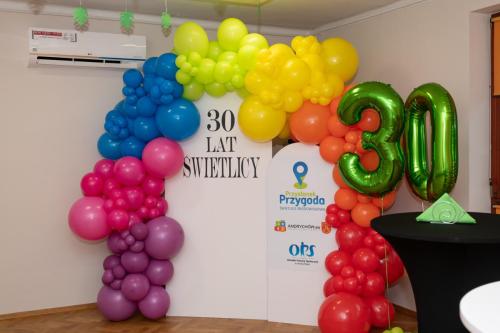 Kolorowe balony wokół napisu "30 lat Świetlicy" i logotypów: Świetlicy Środowiskowej "Przystanek Przygoda", Gminy Andrychów i Ośrodka Pomocy Społecznej w Andrychowie, obok balony w kształcie liczby 30