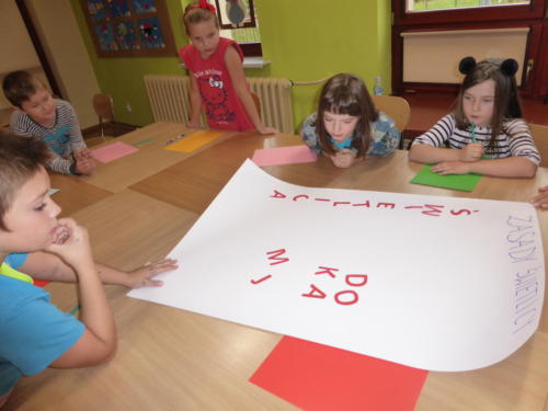 Dzieci układają na kartonie litery, z których stworzą napisy, na szczycie kartki nagłówek "Zasady świetlicy"