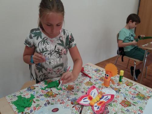 Dzieci robią zwierzęta z papieru - dziewczynka przykleja elementy żaby, chłopiec wycina coś z papieru