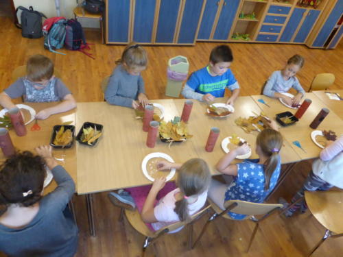 Dzieci siedzą wokół stołu i robią korony drzew z jesiennych liści