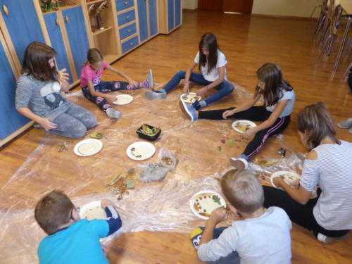 Dzieci układają liście i żołędzie na papierowych talerzykach